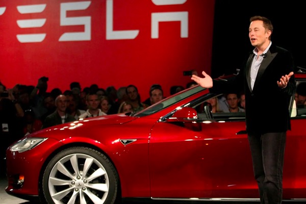 Elon Musk in front of a red Tesla